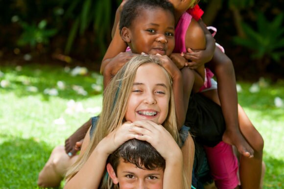 Multiracial children playing together forming human pile in garden.